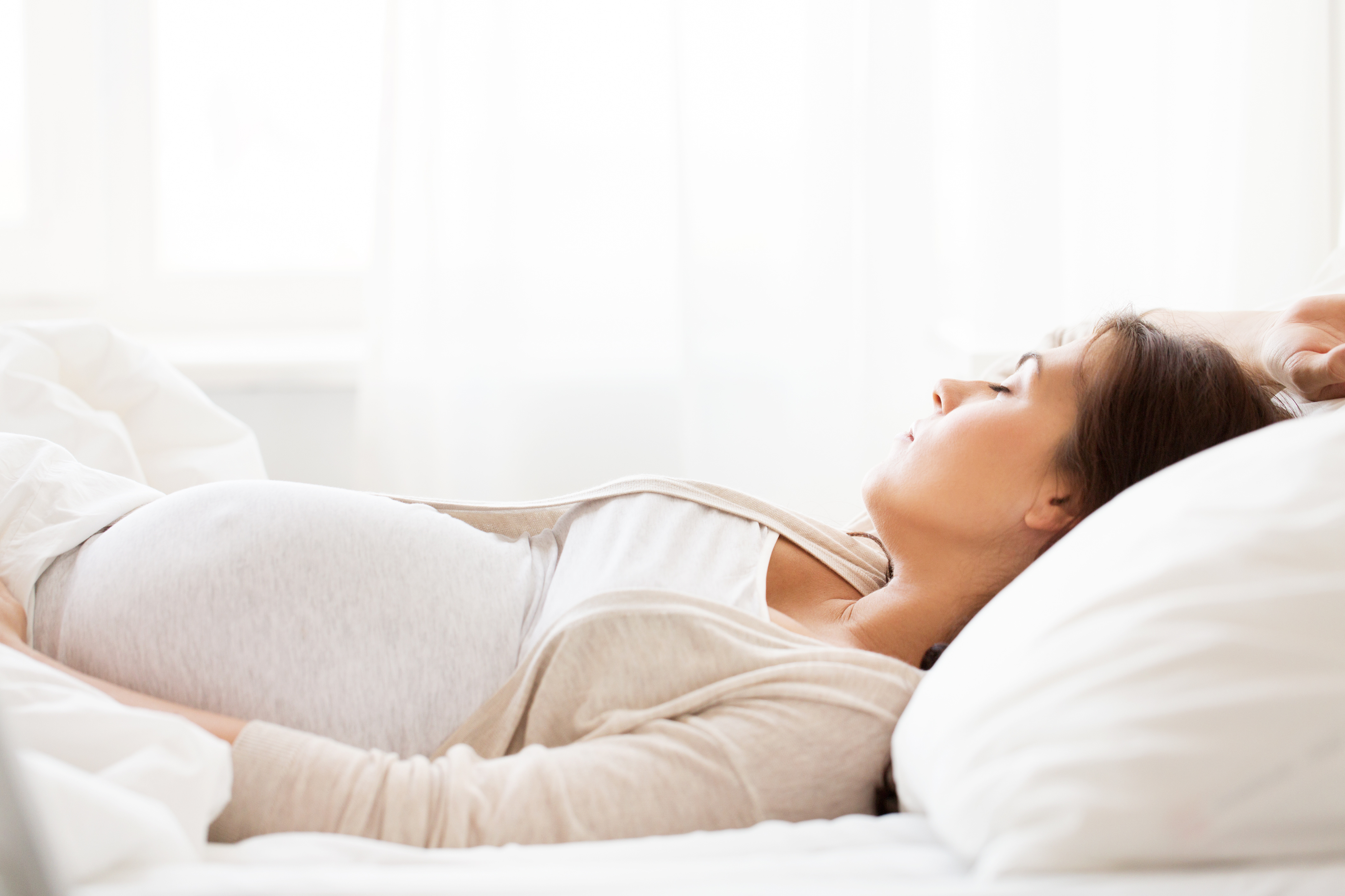 Pregnant woman wearing light colors laying down in bed sleeping