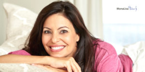 Woman with brown hair, wearing pink shirt, smiling, leaning on pillow on "MonaLisa Touch" ad