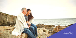 A couple sitting on rocks at the beach covered with a blanket on purple "MonaLisa Touch" ad