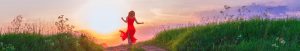 Landscaped image of woman wearing bright red dress in a field during sunset