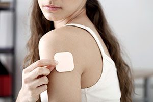 Woman wearing white tank putting a birth control patch on her shoulder