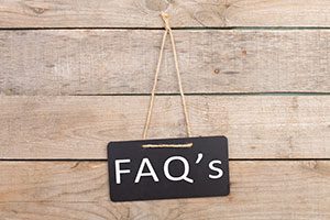 Chalkboard sign hanging from string displaying "FAQ's" text against wood background