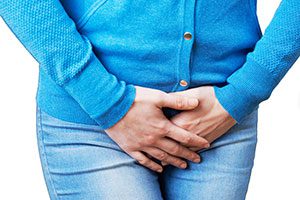 Woman wearing jeans and a blue cardigan holding bladder area in pain